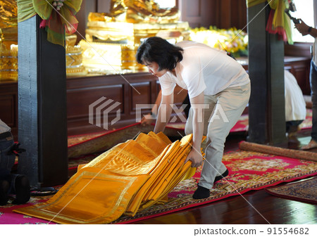 Asian Man supports and prepares orange monk seat on the red carpet in wood pavilion temple. 91554682