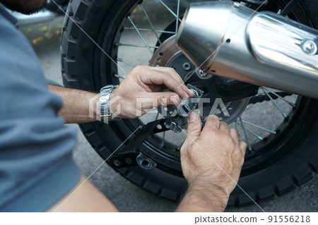 close up technician worker hand, fixed motocycle wheel at the outside of garage. close up technician worker hand, fixed motocycle wheel at the outside of garage. 91556218