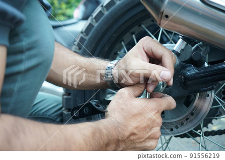 close up technician worker hand, fixed motocycle wheel at the outside of garage. close up technician worker hand, fixed motocycle wheel at the outside of garage. 91556219