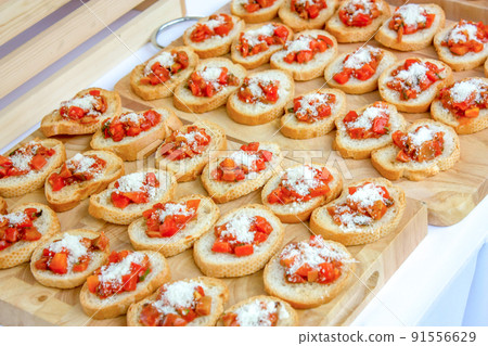 Baked slided French breads are arranged on the wood Butcher, topping by cheese and cooked tomato cube., Read to serve. Baked slided French breads are arranged on the wood Butcher, topping by cheese and cooked tomato cube., Read to serve. 91556629