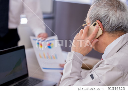 A busy senior man reading documents while talking on a business smartphone 91556823