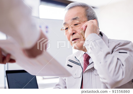 一位忙碌的老人一邊用商務智能手機交談一邊閱讀文件 91556860