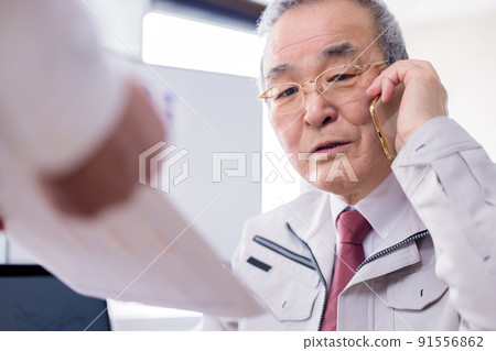 一位忙碌的老人一邊用商務智能手機交談一邊閱讀文件 91556862