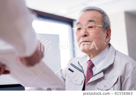 一位忙碌的老人一邊用商務智能手機交談一邊閱讀文件 一位忙碌的老人一邊用商務智能手機交談一邊閱讀文件 91556863