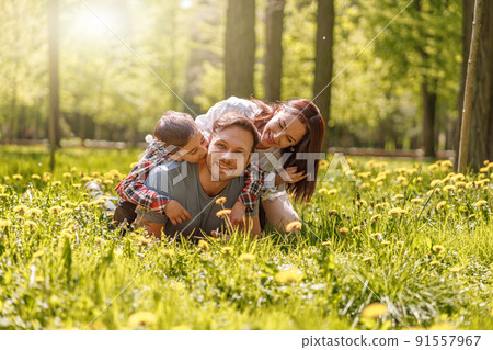 Portrait of happy Caucasian family lying in hugs on green grass in park on sunny summer day. 91557967