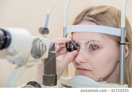 A male ophthalmologist checks the eyesight of a young girl using a modern device with a light beam A male ophthalmologist checks the eyesight of a young girl using a modern device with a light beam 91558305