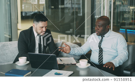 Angry businessman in shirt an tie criticizes severely his partner during meeting in modern cafe. Irritated african american boss gesticulates emotionally and agressively talking with colleague Angry businessman in shirt an tie criticizes severely his partner during meeting in modern cafe. Irritated african american boss gesticulates emotionally and agressively talking with colleague 91558951