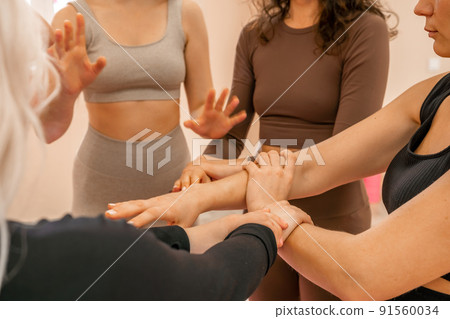 Partnership and unity concept: unrecognizable women in sportswear holding wrists of each other, forming circle. Group of happy young women holding hands. Side view on human hands. Partnership and unity concept: unrecognizable women in sportswear holding wrists of each other, forming circle. Group of happy young women holding hands. Side view on human hands. 91560034