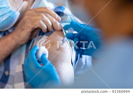 Biracial female health worker giving an injection to caucasian senior man at home 91560994