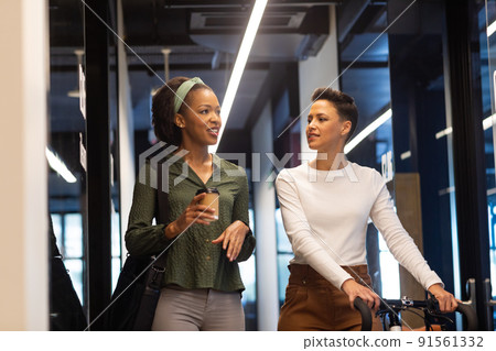 Biracial businesswoman with bicycle discussing with african american colleague in corridor of office Biracial businesswoman with bicycle discussing with african american colleague in corridor of office 91561332