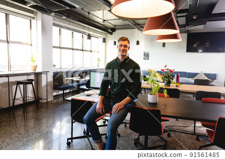 Portrait of smiling young caucasian businessman sitting on desk in office Portrait of smiling young caucasian businessman sitting on desk in office 91561485