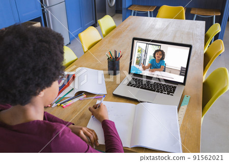 African american girl writing in notebook while taking notes from friend though video call on laptop African american girl writing in notebook while taking notes from friend though video call on laptop 91562021