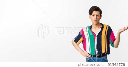 Confused gay man asking what happened, raising hand aside and looking puzzled at camera, standing over white background 91564776