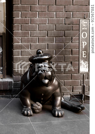 Decorative statue of cute bulldog breed dog sitting near outdoor cafe enter 91567881