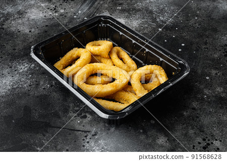 Frozen raw squid or onion rings breaded, on black dark stone table background 91568628