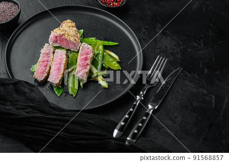 Homemade Cut Grilled Sesame Tuna steak with spring onions and sugar snap peas , on plate, on black stone background , with copyspace  and space for text 91568857