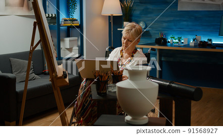 Senior woman with chronic impairment using laptop to draw vase sketch on white canvas. Wheelchair user with disability and health condition drawing masterpiece with computer for inspiration. Senior woman with chronic impairment using laptop to draw vase sketch on white canvas. Wheelchair user with disability and health condition drawing masterpiece with computer for inspiration. 91568927