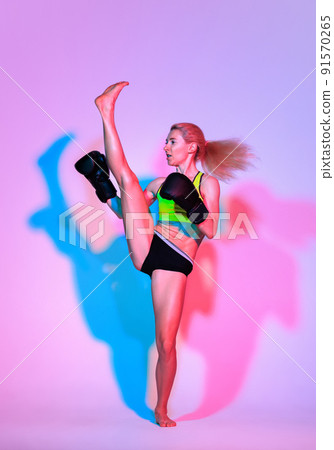 One young woman, female professional kickboxer in sports uniform and gloves training isolated on dark green background in neon. One young woman, female professional kickboxer in sports uniform and gloves training isolated on dark green background in neon. 91570265