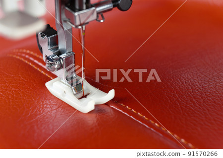 Modern sewing machine presser foot with a needle sews red leather 91570266