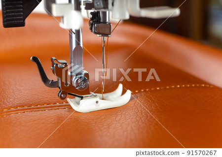 Modern sewing machine presser foot with a needle sews brown leather 91570267