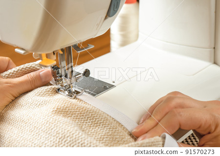 Female hands stitching white fabric on modern sewing machine. Close up view of sewing process. Female hands stitching white fabric on modern sewing machine. Close up view of sewing process. 91570273