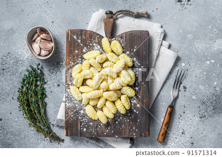Raw homemade potato gnocchi with fork on wooden cutting board. Gray background. Top view Raw homemade potato gnocchi with fork on wooden cutting board. Gray background. Top view 91571314