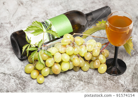 White wine bottle with bunch of grapes, glass on a dark background, top view. 91574154
