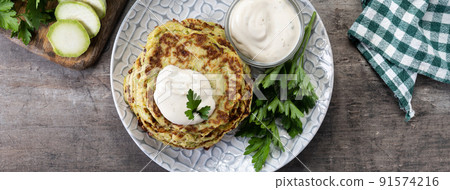 Zucchini fritters with yogurt sauce on wooden table Zucchini fritters with yogurt sauce on wooden table 91574216