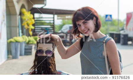 A brunette touches a mannequin of a man's head with her hand, an advertisement for a hairdressing salon, a barbershop A brunette touches a mannequin of a man's head with her hand, an advertisement for a hairdressing salon, a barbershop 91576826