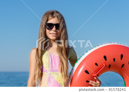 A girl in black glasses holds an inflatable circle in her hand. 91578241