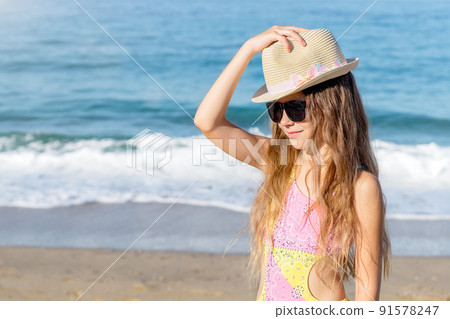 Girl puts a hat on her head on the beach. 91578247