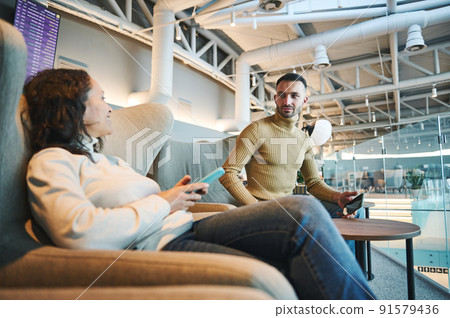 Handsome couple, man and woman chatting while chilling in a VIP lounge of the international airport departure terminal, waiting to board the flight Handsome couple, man and woman chatting while chilling in a VIP lounge of the international airport departure terminal, waiting to board the flight 91579436