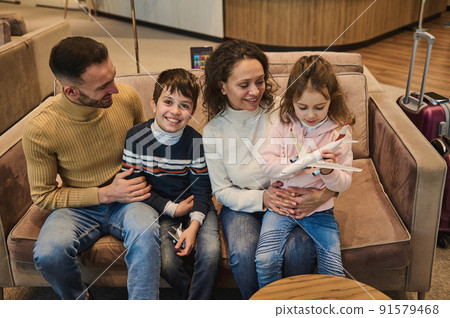 Happy multi-ethnic young loving family spending time together playing toy planes with their kids at the airport while waiting for a flight. Air travel concept 91579468