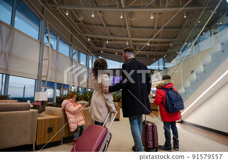 Traveling family with suitcases checking flight information on board with timetable, standing in airport departures terminal, waiting to board flight Traveling family with suitcases checking flight information on board with timetable, standing in airport departures terminal, waiting to board flight 91579557