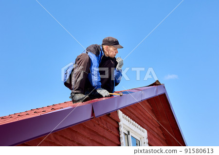Nailing into tin roof while roofing, worker uses hammer to fix roof. Nailing into tin roof while roofing, worker uses hammer to fix roof. 91580613