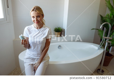 Beautiful young blonde happy woman sitting in bathroom and holding brush cleanser. Beautiful young blonde happy woman sitting in bathroom and holding brush cleanser. 91580712