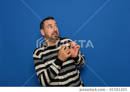 Hispanic bearded man tremendously scared by something next to him, copy space. Isolated on blue studio background. 91581203