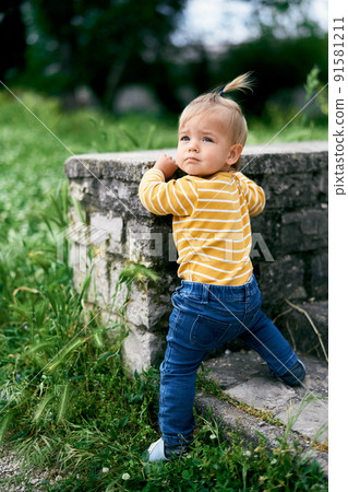 Little girl stands at a stone fence in the park, turning her head Little girl stands at a stone fence in the park, turning her head 91581211