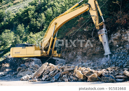 Yellow tracked tractor drills stones near the mountain 91581668