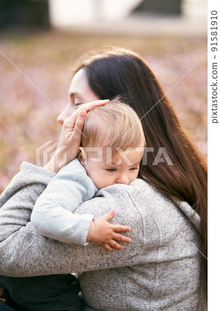 Mom hugs the baby to her chest, sitting on the foliage in the park. Close-up Mom hugs the baby to her chest, sitting on the foliage in the park. Close-up 91581910