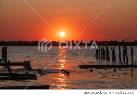 Beautiful red and orange sunset over the sea. The sun goes down over the sea. A flock of cormorants sits on a old sea pier in orange sunset light Beautiful red and orange sunset over the sea. The sun goes down over the sea. A flock of cormorants sits on a old sea pier in orange sunset light 91582158