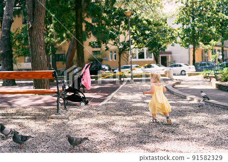 Little girl in a dress walks along the gravel path in the park to the stroller 91582329