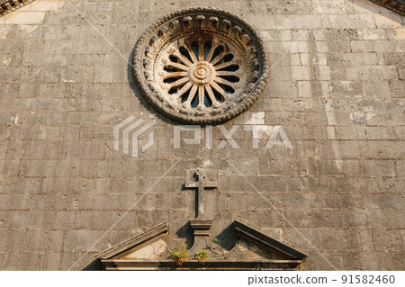 Rose window with ornaments on the dark stone wall of the church above the entrance 91582460