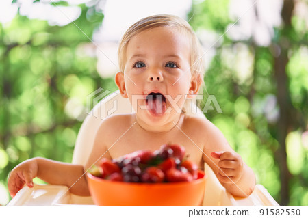 Kid sits at a table in front of a bowl of fruit 91582550