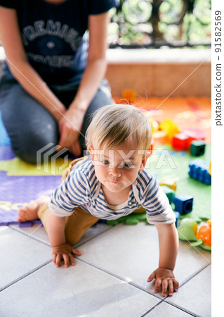 Mom sits on the balcony and a little girl crawls by Mom sits on the balcony and a little girl crawls by 91582569