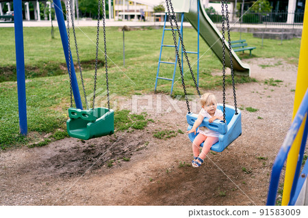 Little girl swinging on a swing in the courtyard of an apartment building Little girl swinging on a swing in the courtyard of an apartment building 91583009