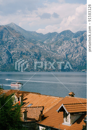 View of the Kotor Bay against the background of mountains above the red-tiled roofs of houses View of the Kotor Bay against the background of mountains above the red-tiled roofs of houses 91583126