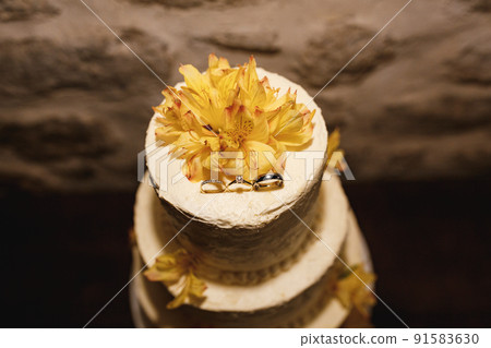 White wedding cake decorated with rings and yellow lilies. Top view 91583630