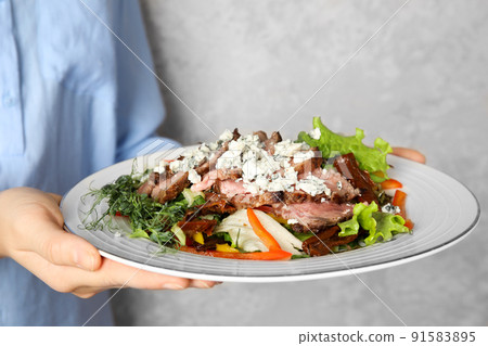 Woman holding plate with delicious salad on grey background, closeup Woman holding plate with delicious salad on grey background, closeup 91583895
