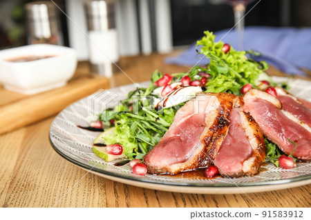 Delicious salad with roasted duck breast served on wooden table indoors, closeup 91583912